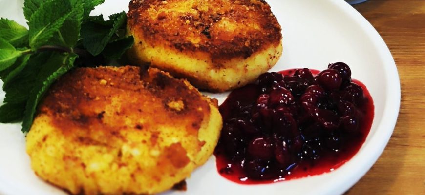 Два кето-сырника с румяной корочкой и ложкой клюквенного варенья на светлой тарелке. Низкоуглеводная подача без сахара.